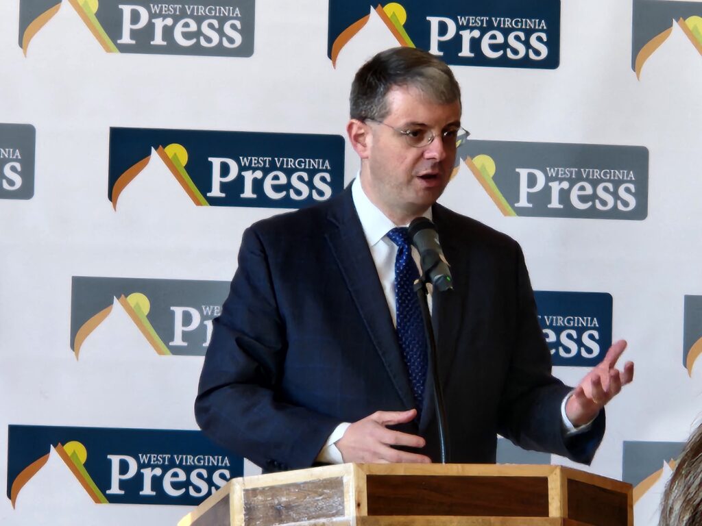 Man talks at a podium with a back drop that says West Virginia press.