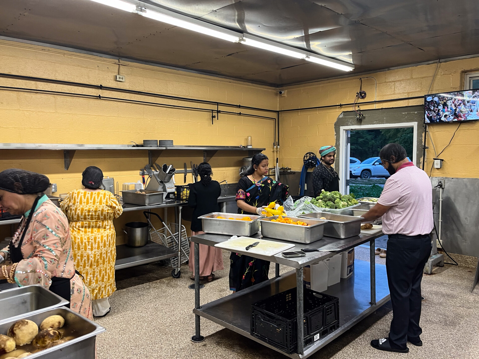 Six people, three women and two men, prepare food in a yellow kitchen.