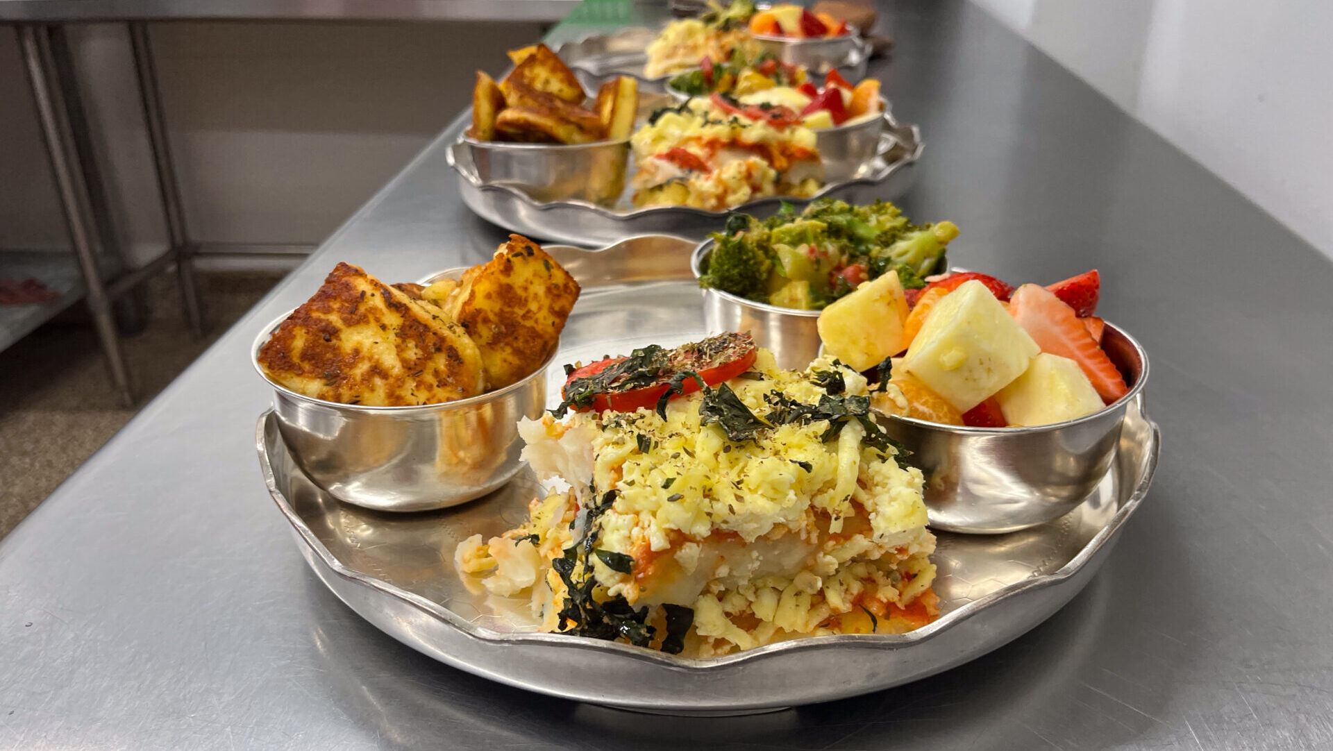 A plate of fruits, vegetables and other prepared foods on a metal countertop in a kitchen.