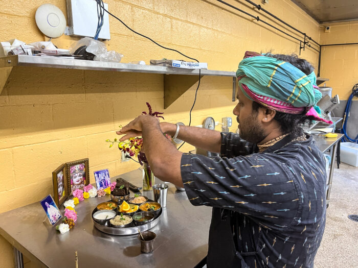 A man with a blue headwrap standing behind a plate of food in front of photos.