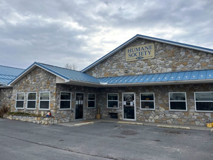 A stone building with a blue angular roof is labeled "Humane Society" with a sign at its top.