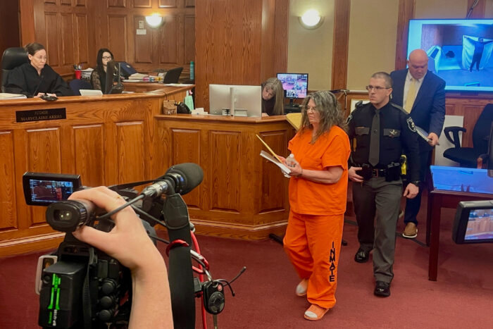 A woman in an orange jumpsuit is led away by officers in a court room.