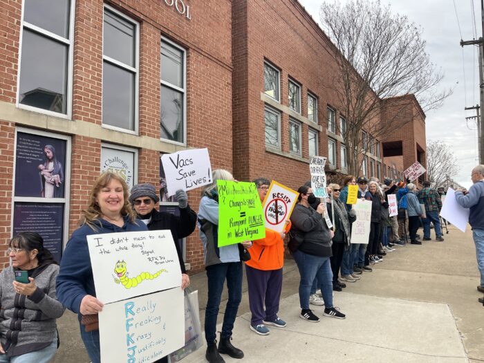 A line of people outside a red brick building hold up signs.