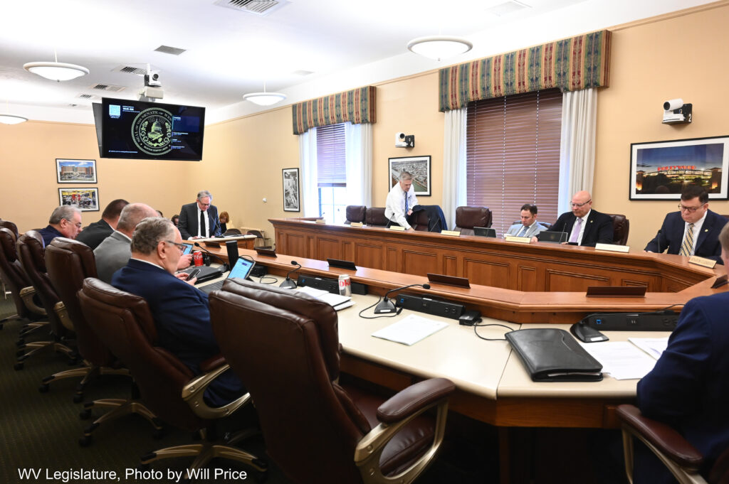 A large U-shaped desk has many empty seats but many suited men sitting in large office chairs.