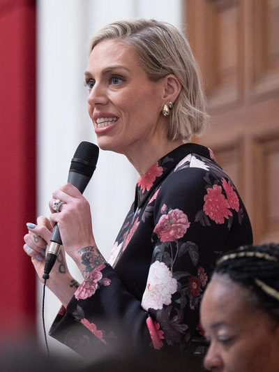 A woman stands and speaks into a microphone.