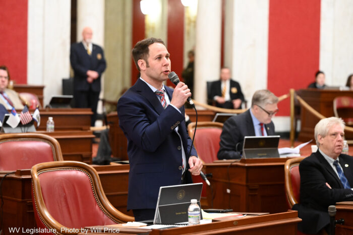 A man in a legislative chamber stands and speaks to a bill.