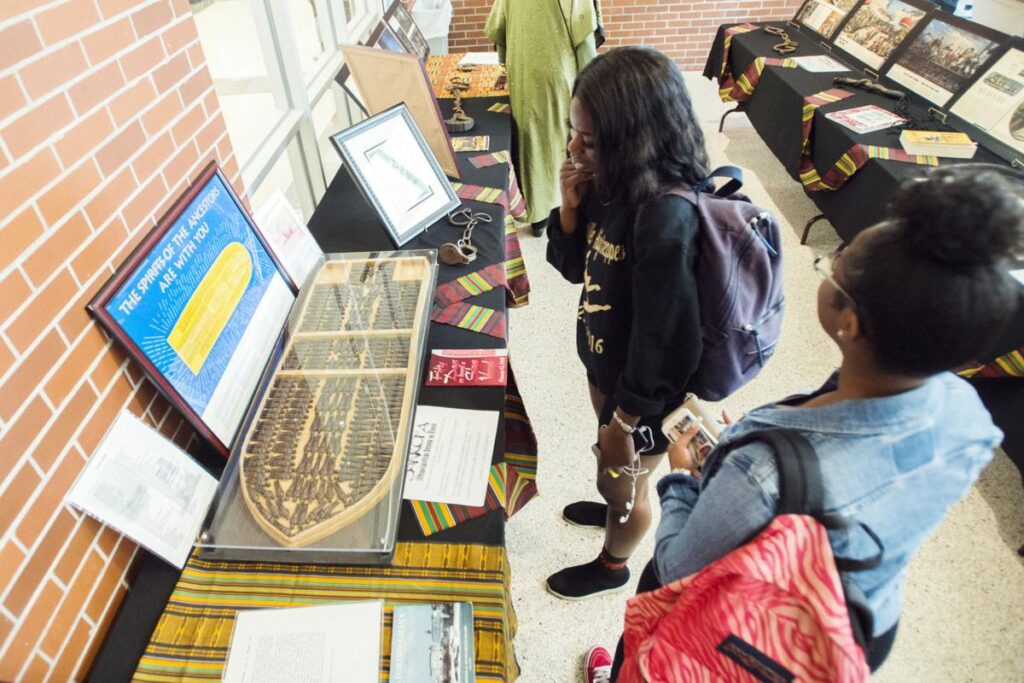 Teenagers stand around tables displaying artifacts and informational plaques, observing them.