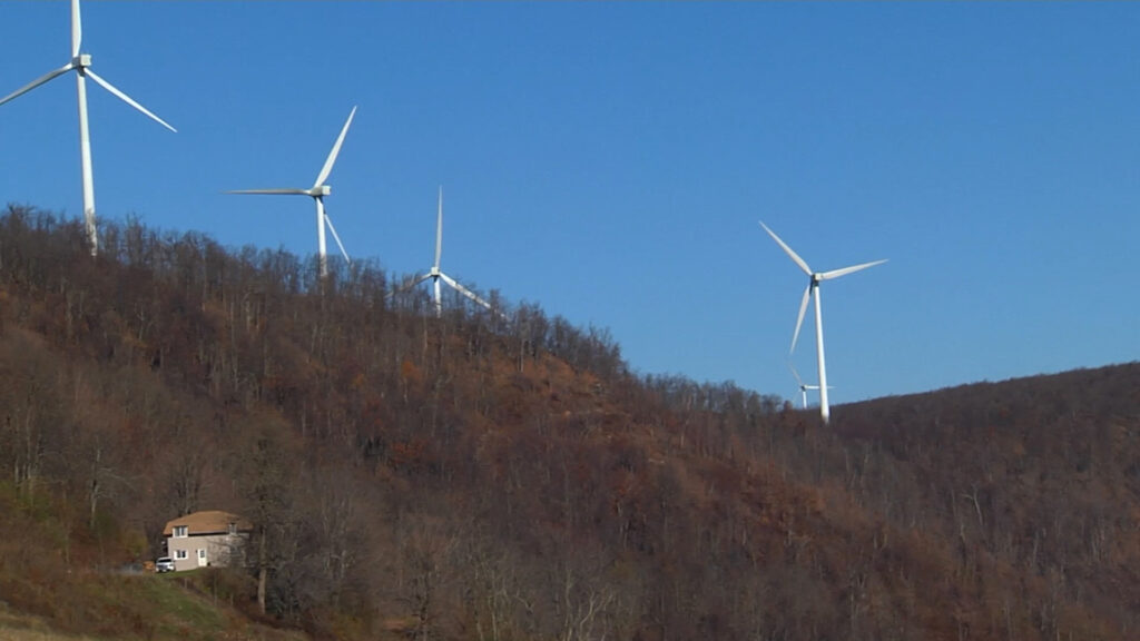 Three wind turbines spin atop a wooded, leafless ridge against a clear blue sky.