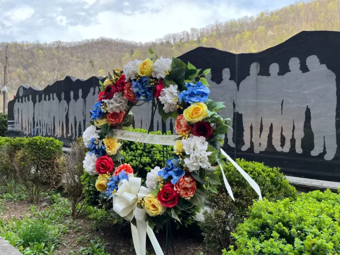 A wreath of flowers is shown in front of a memorial.