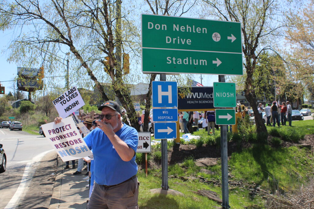 people standing under street signage hold handmade signs
