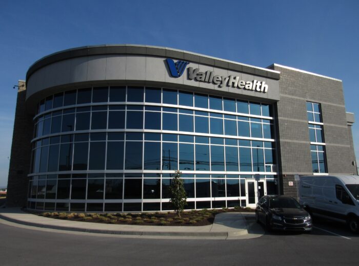 A gray building with tall glass panes has a sign on it that reads "Valley Health."