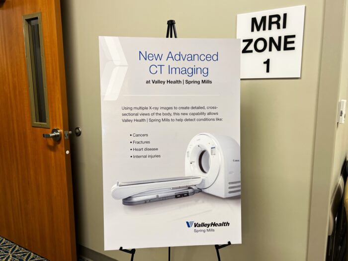 A sign in a medical office hallway reads "New Advanced CT Imaging at Valley Health" and displays the image of a white MRI machine.