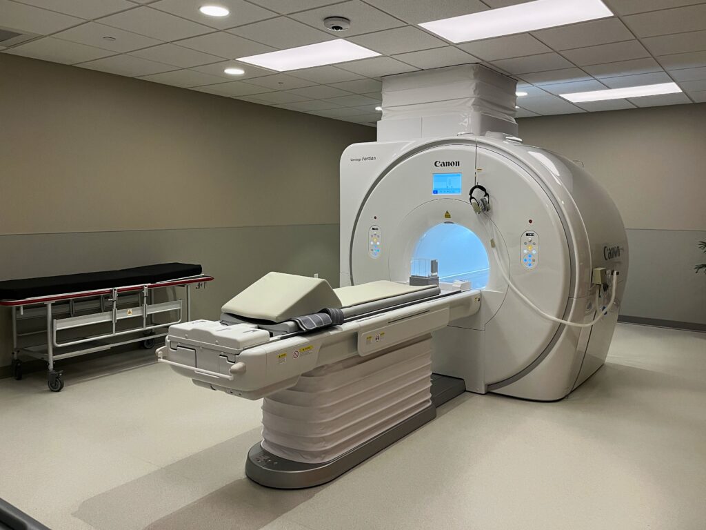 A large, sleek, white CT scan machine sits in a sterile white room.