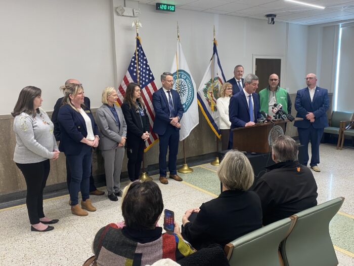 Man at podium surrounded by people. Man is speaking to an audience.