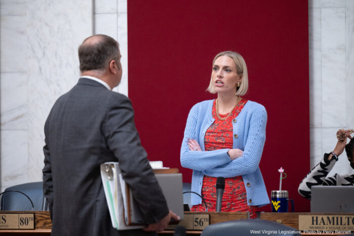 A woman stands with arms crossed talking to a man.