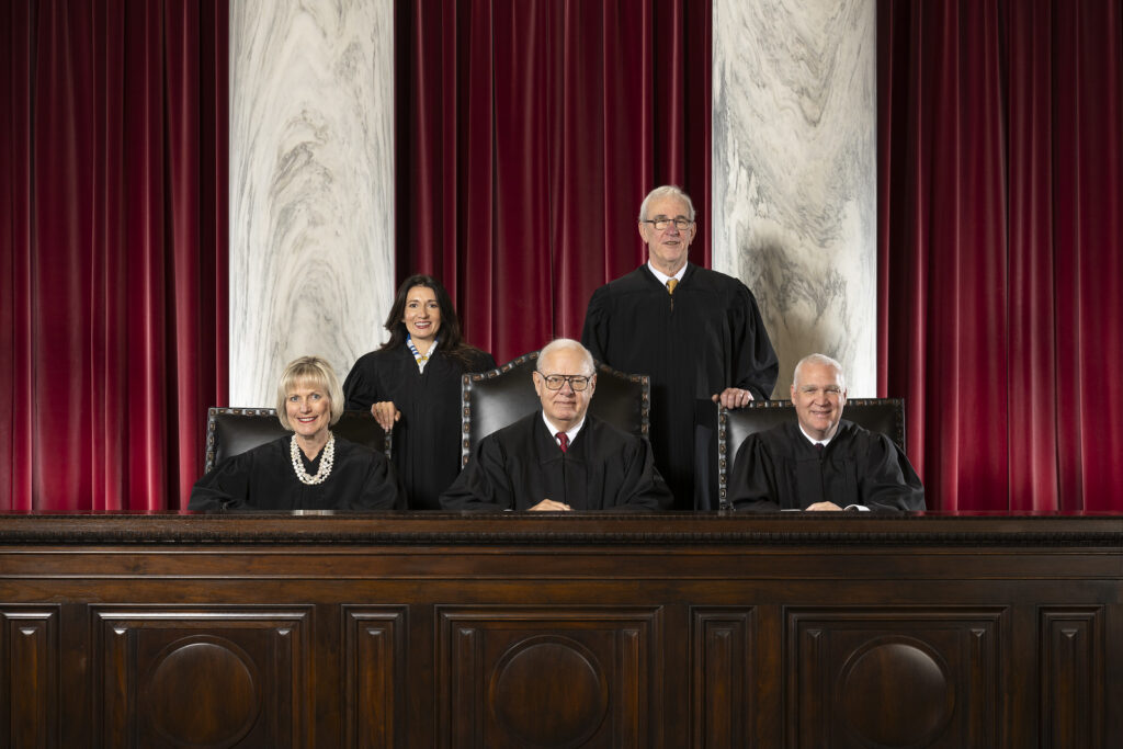 Three men and two women in long black robes pose for a portrait. Two men and a woman are seated.