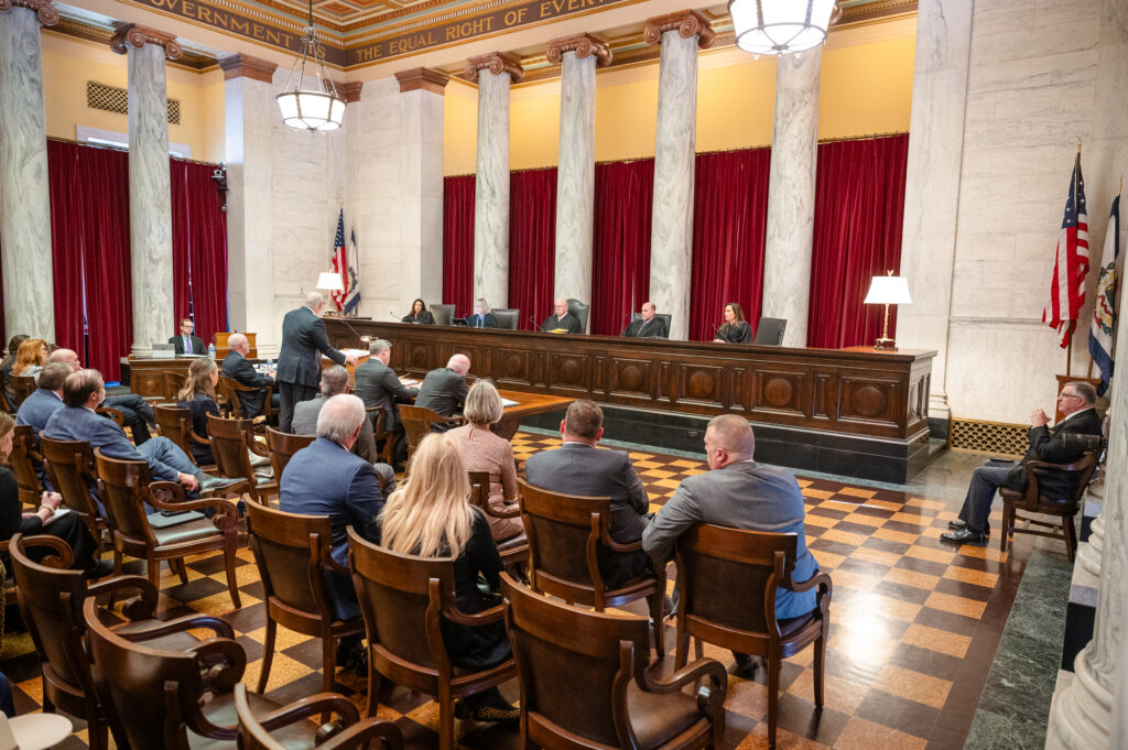 A crowd looks at a row of five people dressed in robes behind a high desk.