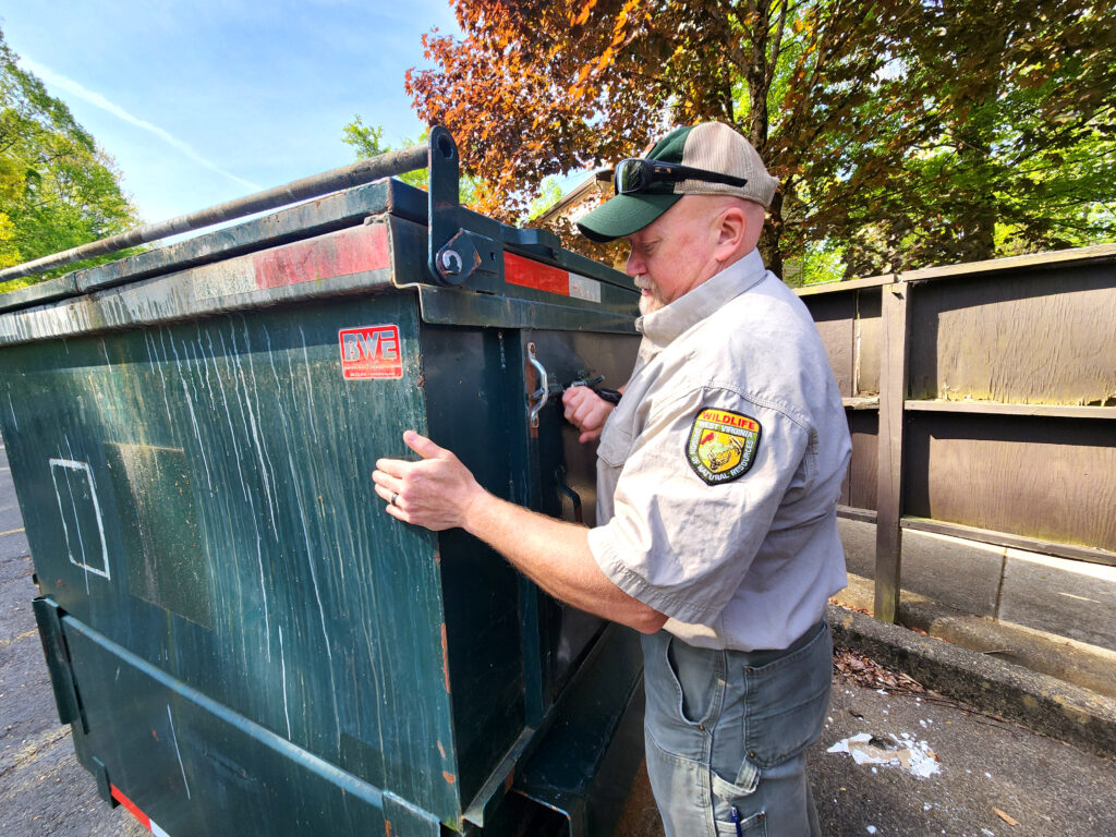 Man in uniform standing beside a green trash dumpster