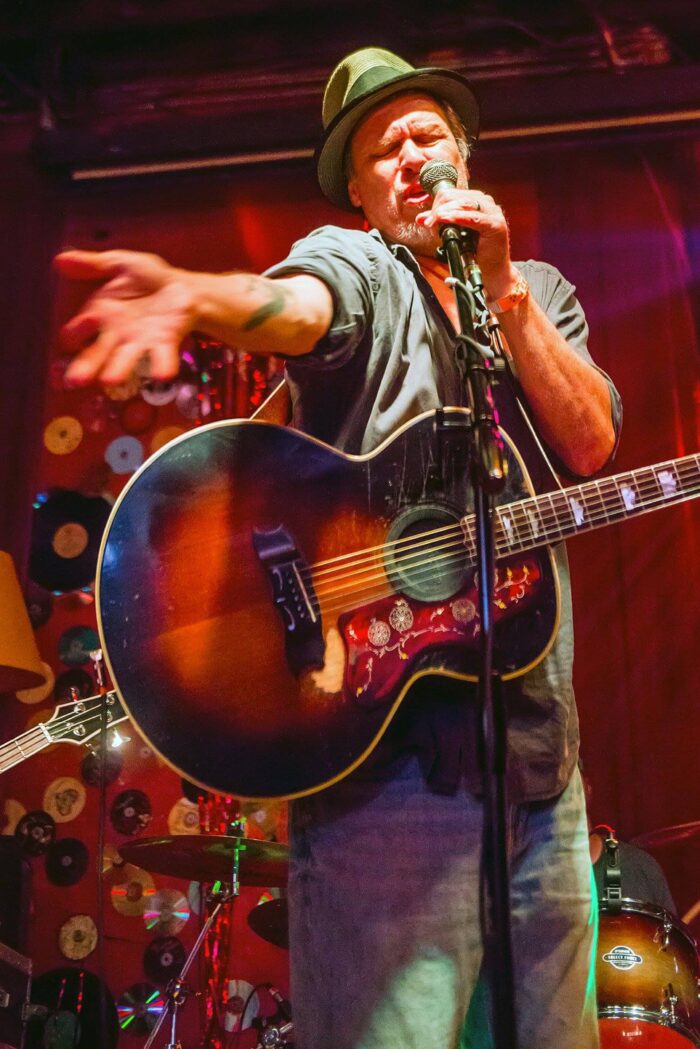 A white man playing guitar and singing into a microphone.