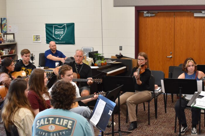 A group of high school students play music with their teacher.