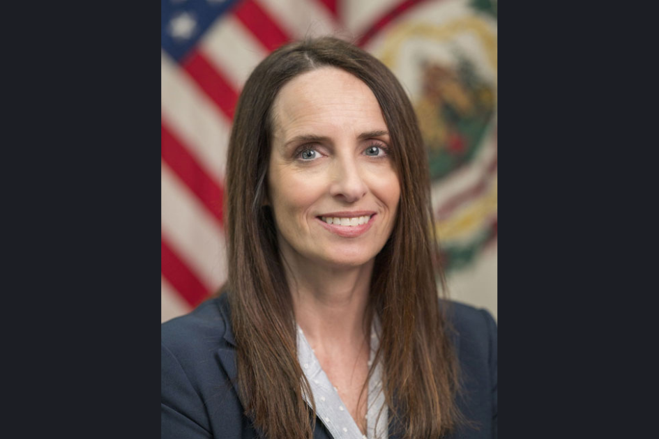 A woman in formal attire smiles for a portrait photo, seated before the American and West Virginia flags.