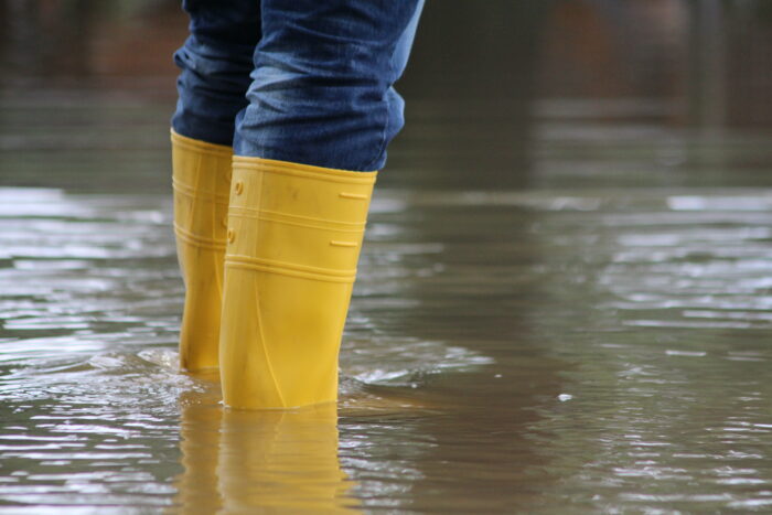 A closeup photo of a person wearing yellow rain boots in flood waters.