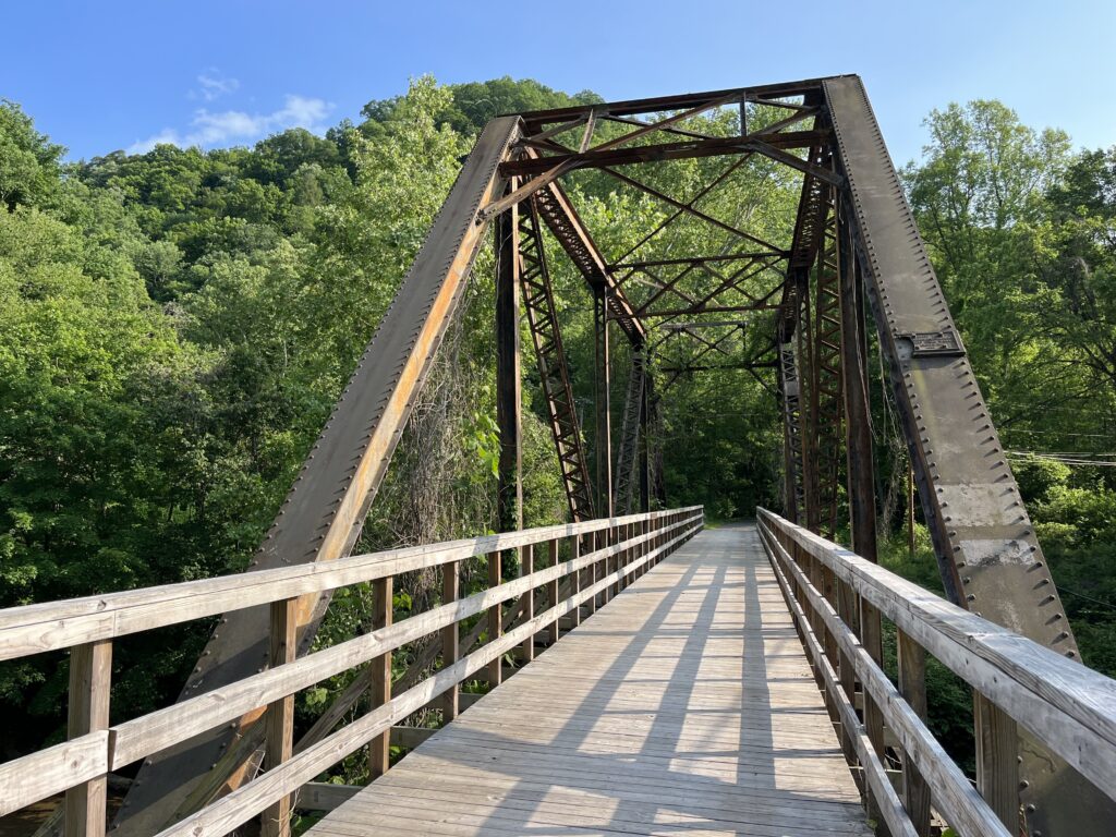 A wooden bridge with scaffolding crosses into a wooded area.