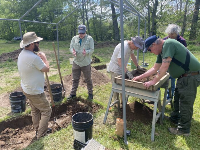 A group of people working at dirt sifter tables searching for artifacts