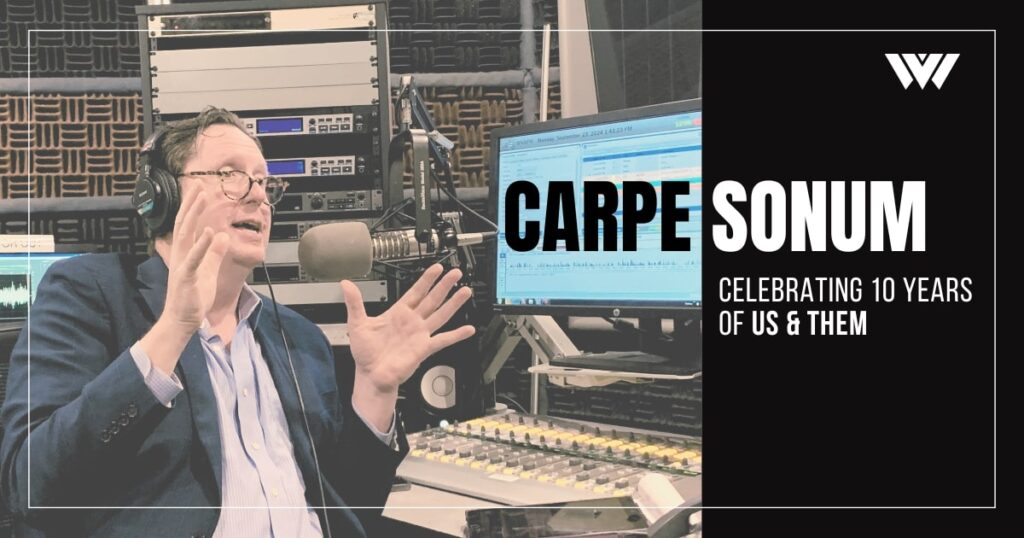 Trey Kay, a white man with brown hair wearing a blue blazer jacket and a light blue button up, recording a podcast episode at a recording booth with the words "Carpe Sonum, Celebrating 10 years of Us & Them" written on the image.