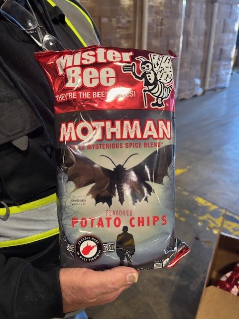 A man holds a bag of Mister Bee "Mothman" chips in a warehouse.
