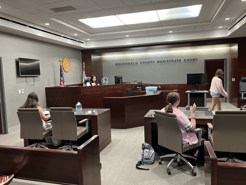 A group of teens sit in a court room filling the roles of judge, jury and attorney