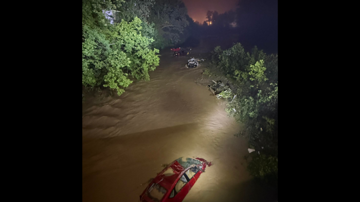 Floodlights illuminate badly damaged cars in a flooded waterway at night