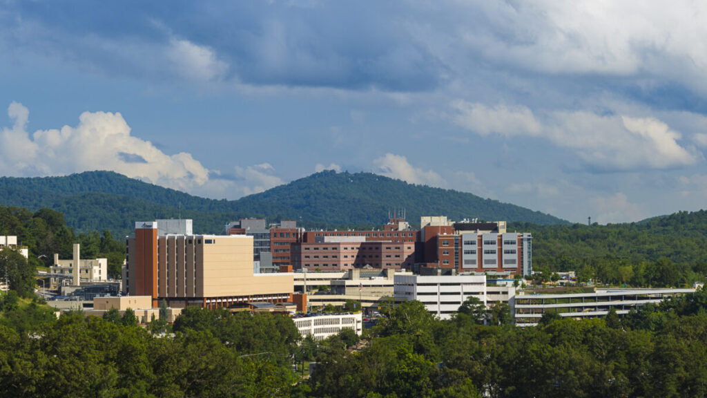 An elevated view of a hospital surrounded by green hills.