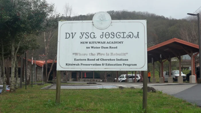 A sign outside of a building that reads, "New Kituwah Academy" in the Cherokee and English languages.