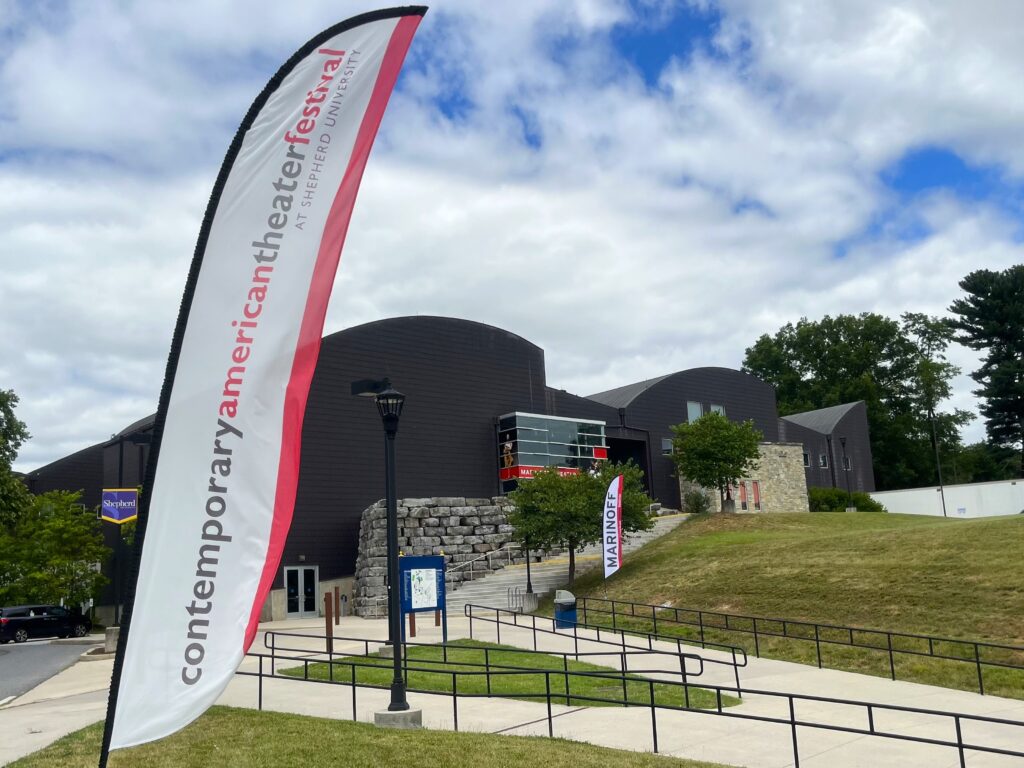 Outside a large, wood-panel building, a red and white banner reads "Contemporary American Theater Festival."