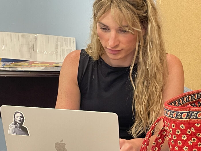 A transgender woman with long blond hair works from her laptop.