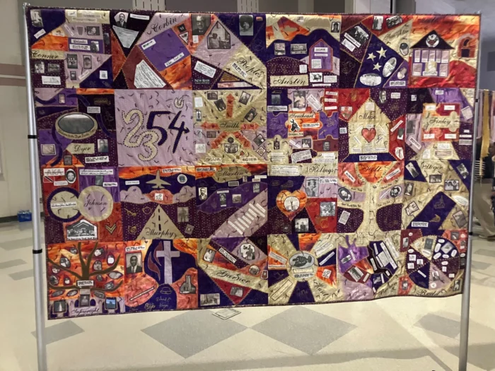An image of a quilt. The colors are warm, with reds, purples, yellows and oranges.
