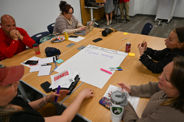 A group sits around a table with a large piece of paper in the middle and markers arrayed in front of them