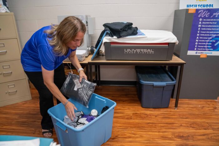 A woman wearing a blue shirt and black pants pulls resources out of a storage tub in a classroom.