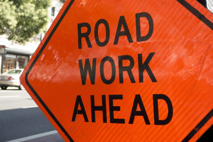 large orange sign with the words Road Work Ahead