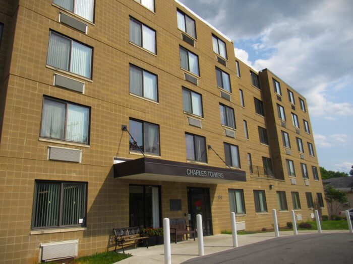 An apartment complex on the end of a driveway with numerous windows displays the words "Charles Towers."