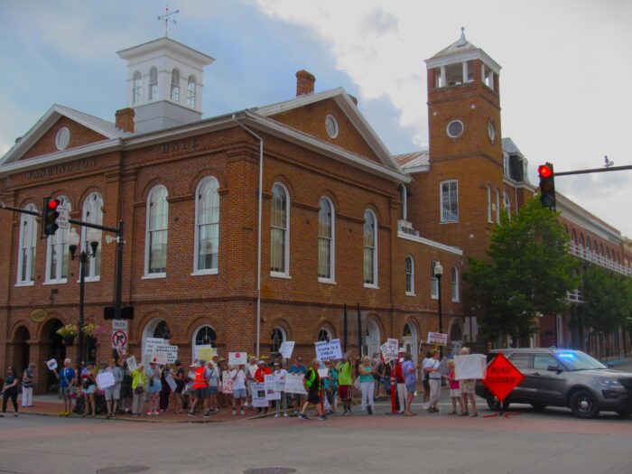 People holding picket signs stand along a downtown road, waving the signs for drivers.
