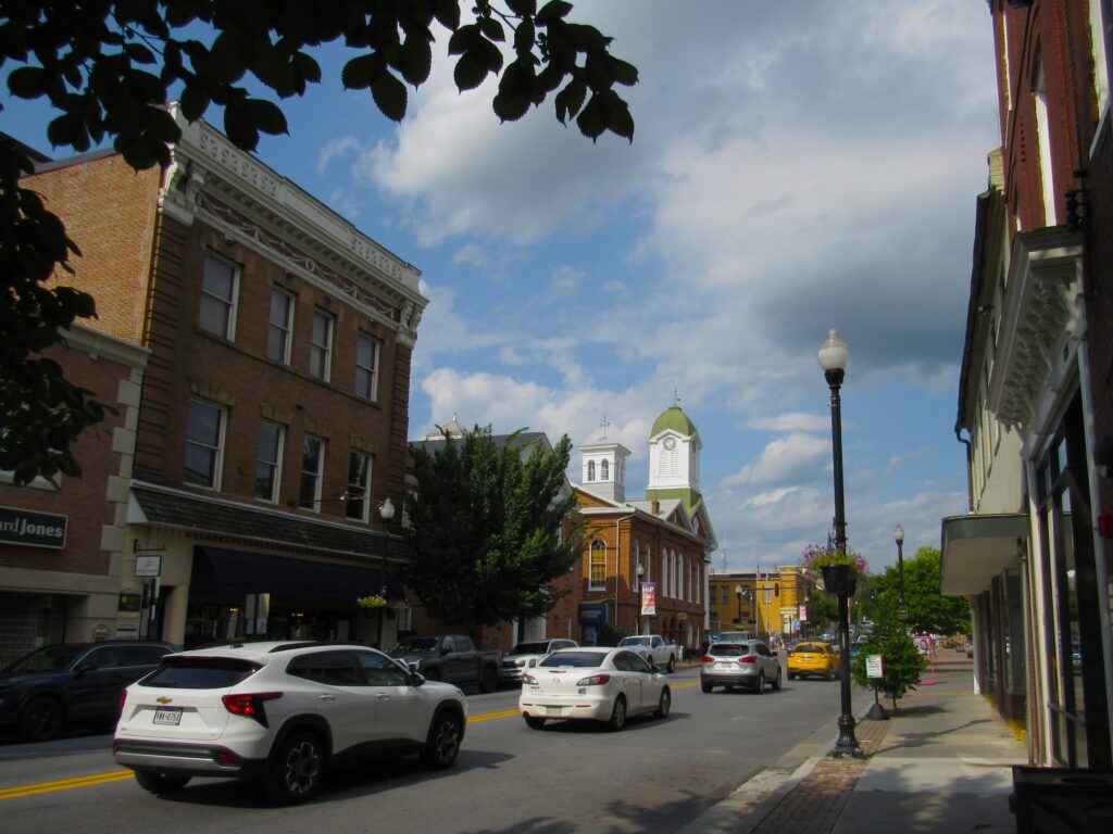 Cars drive along a downtown city street. In the distance, the dome of the Jefferson County Courthouse is visible.