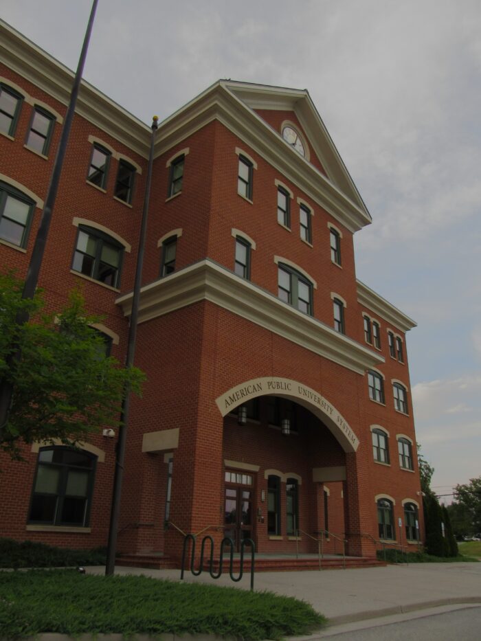 A red brick building with a clock tower displays text in an arch over the doorway that reads "American Public University System."