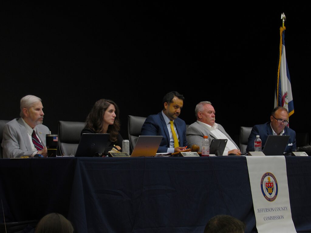 Five people in formal attire sit at a desk with microphones and a banner that reads "Jefferson County Commission."