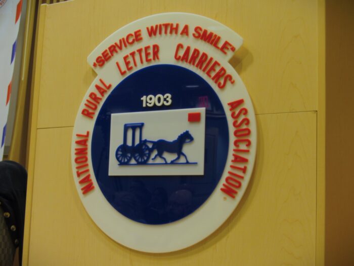 A logo on a podium reads "Service With A Smile: National Rural Letter Carriers' Association."