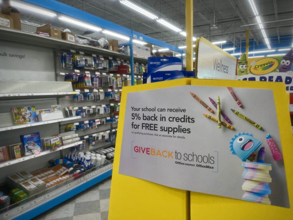 A back-to-school display at an office supply store stands before shelving that contains office supplies.