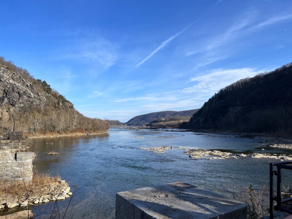 Two rivers converge against the backdrop of mountainsides covered with barren trees. Small rocks and man-made stone fixtures poke out from parts of the river.