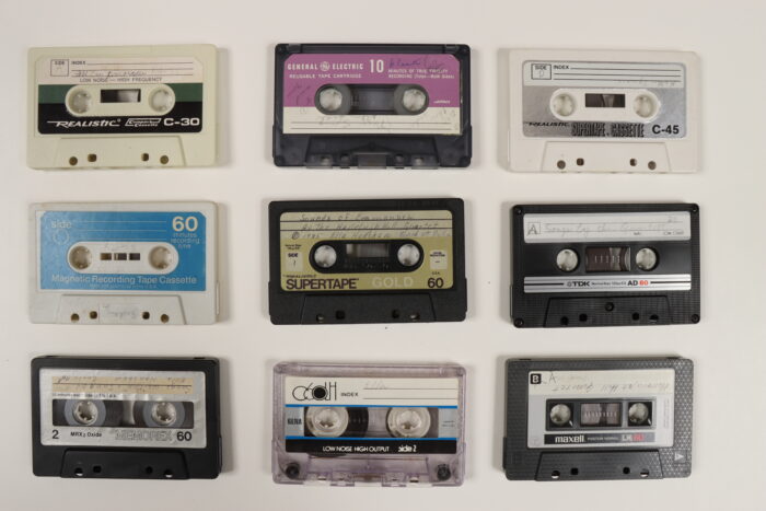 Nine cassette tapes of different colors photographed against a white background.