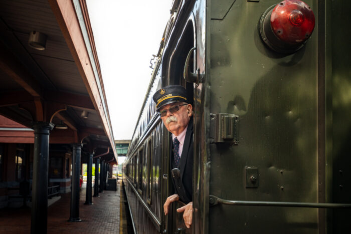 A white man poking his head out of a train near a train platform.